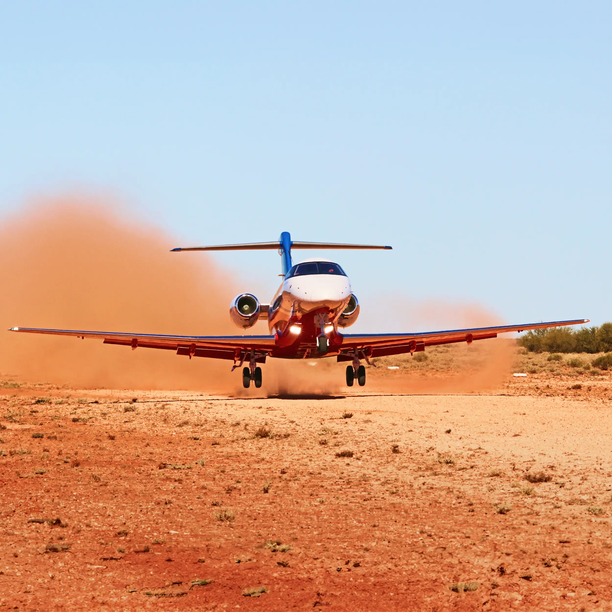 A PC-24 RFDS takes off from a rough airstrip in the wilderness, kicking up dust.