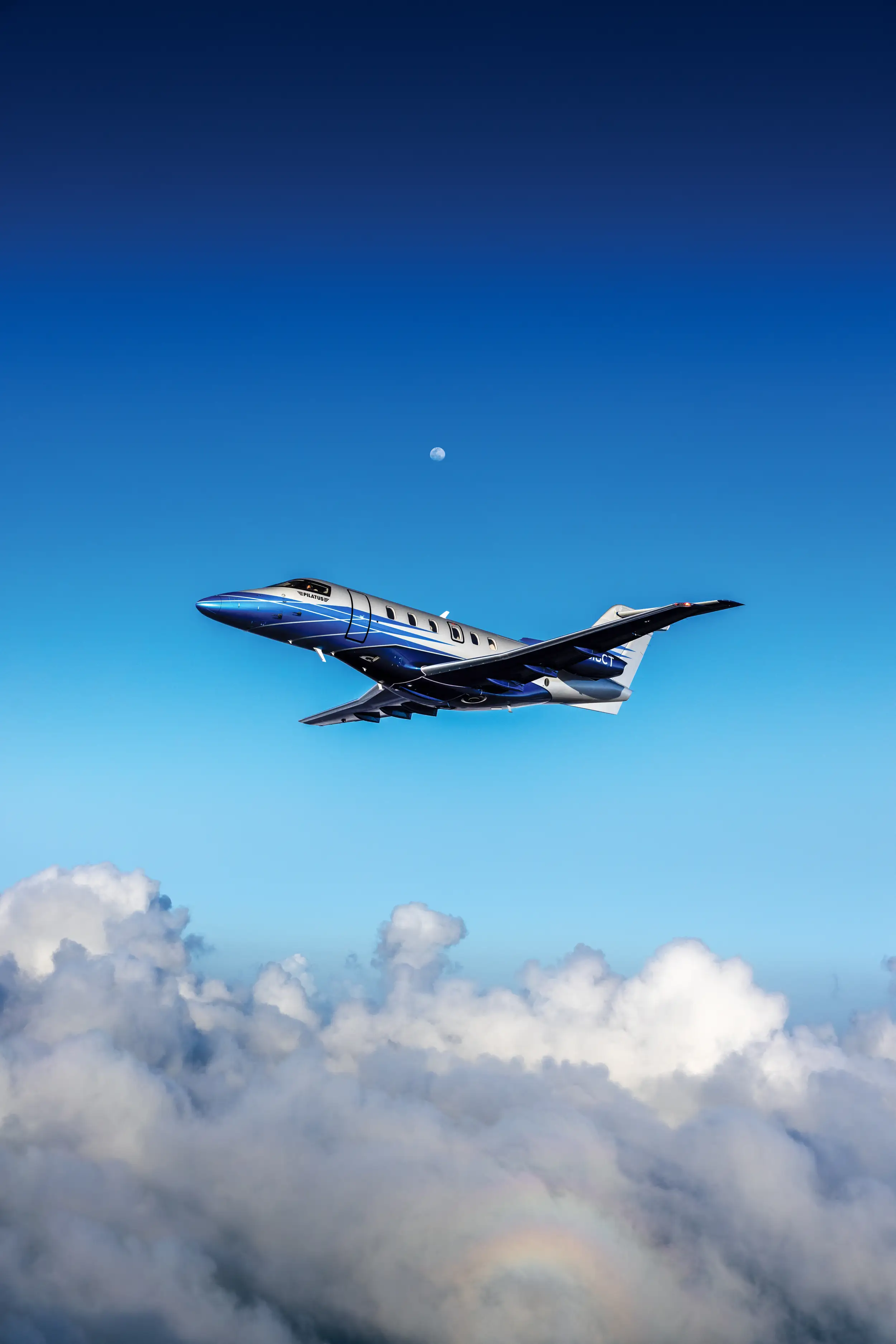 A PC-24 flies over a sea of fog, with the blue sky and the moon in the background